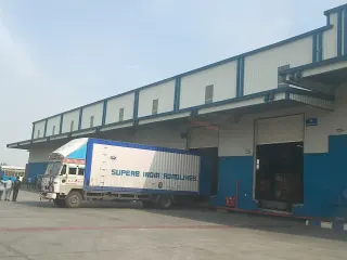 Warehouse loading dock exterior with trucks, workers, open dock doors and a paved apron.