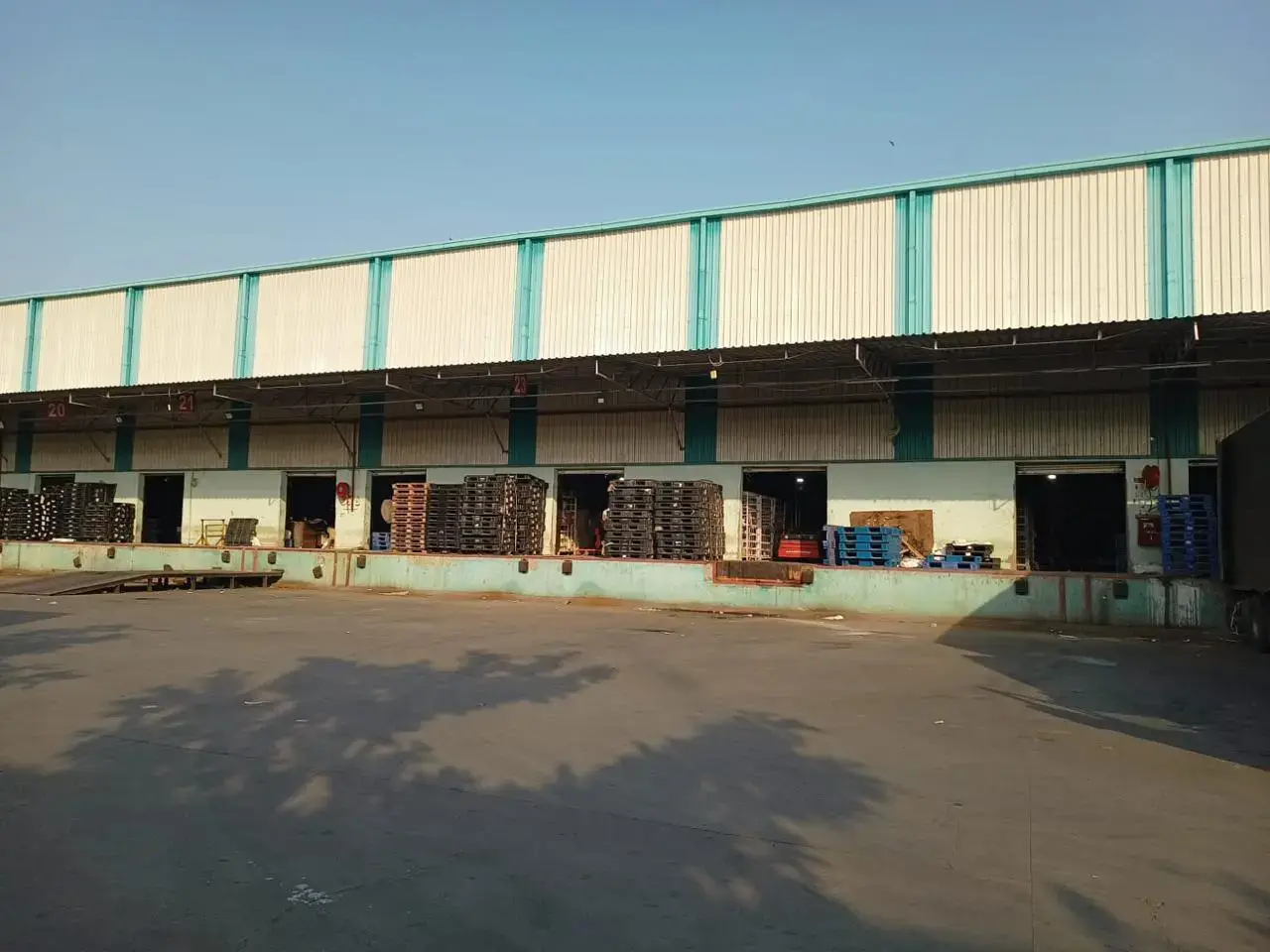 Warehouse loading facade with multiple open bays, stacked pallets, and a paved apron in front.
