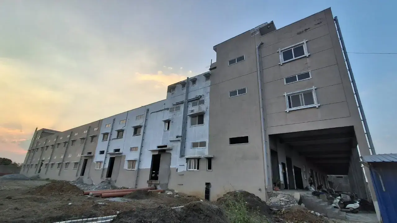 Exterior view of a multi-storey industrial building with unfinished ground, construction debris, windows, and a covered loading entrance.