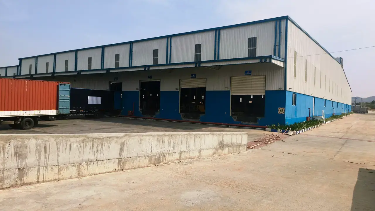 Exterior view of a blue-and-white warehouse with loading dock doors, concrete apron, truck trailer, and open yard.